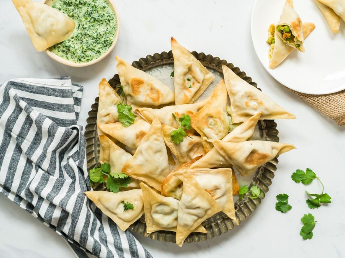 Baked samosa filled with potato, cauliflower, and peas on a plate with cilantro and mint dipping sauce.