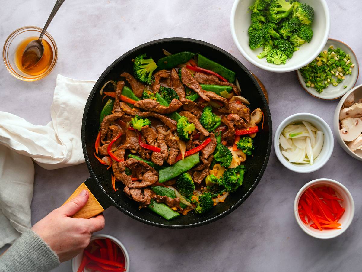 Beef stir fry with tender strips of beef with broccoli, carrots, bell peppers, and snow peas in soy stir fry sauce in a skillet.