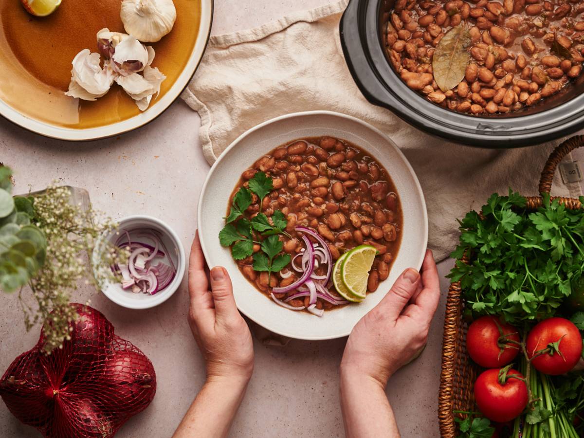Crockpot pinto beans in a bowl with red onions, cilantro, lime slices, and other vegetables.