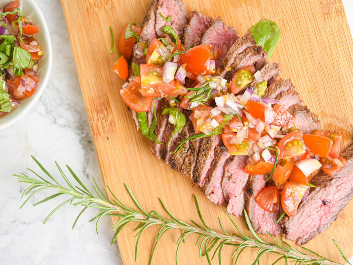 Grilled steak on a wooden board with tomato, and basil salad.