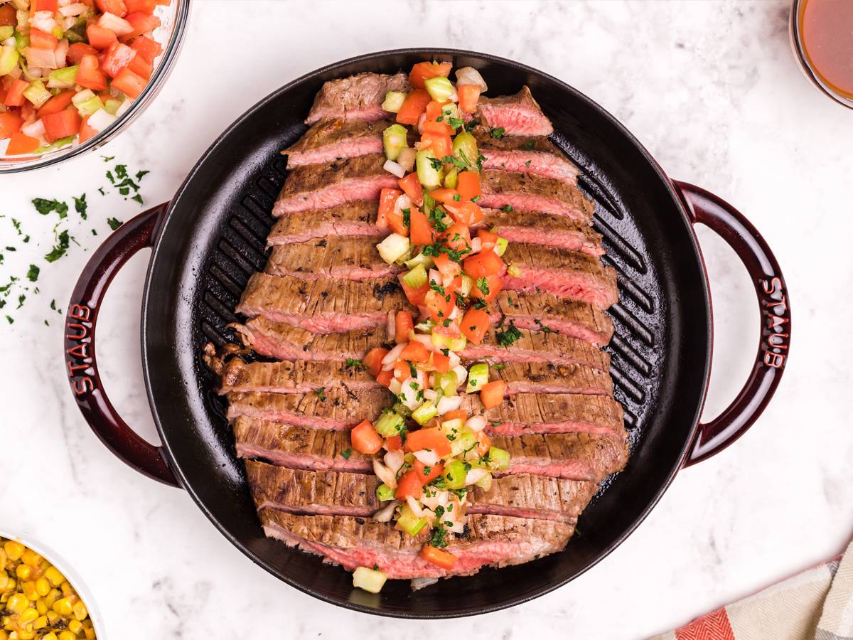 Marinated flank steak served with a tomato, celery, and onion salsa on a grill pan.