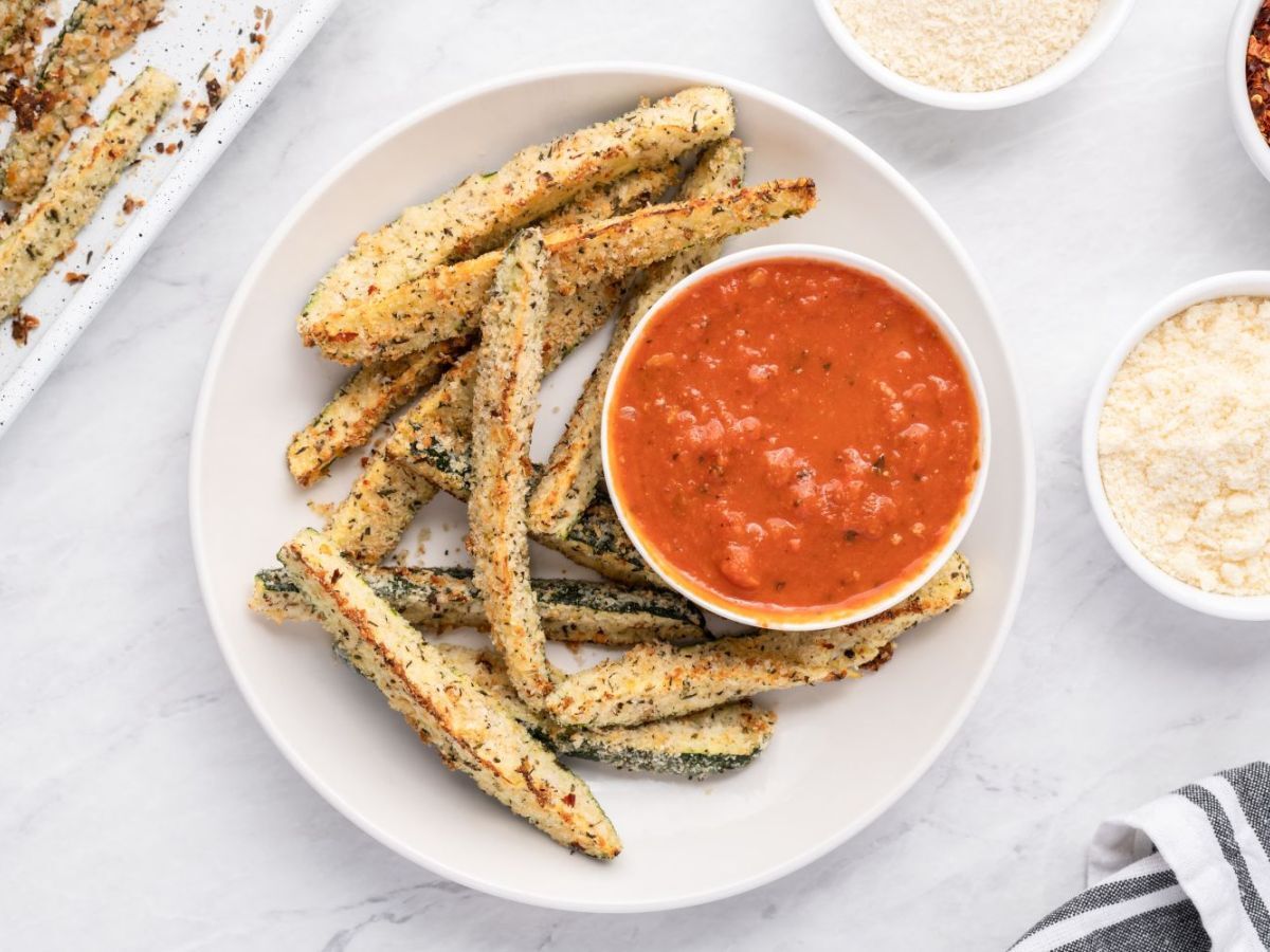 Baked Parmesan zucchini fries with a crispy panko breading on a white plate with marinara sauce.