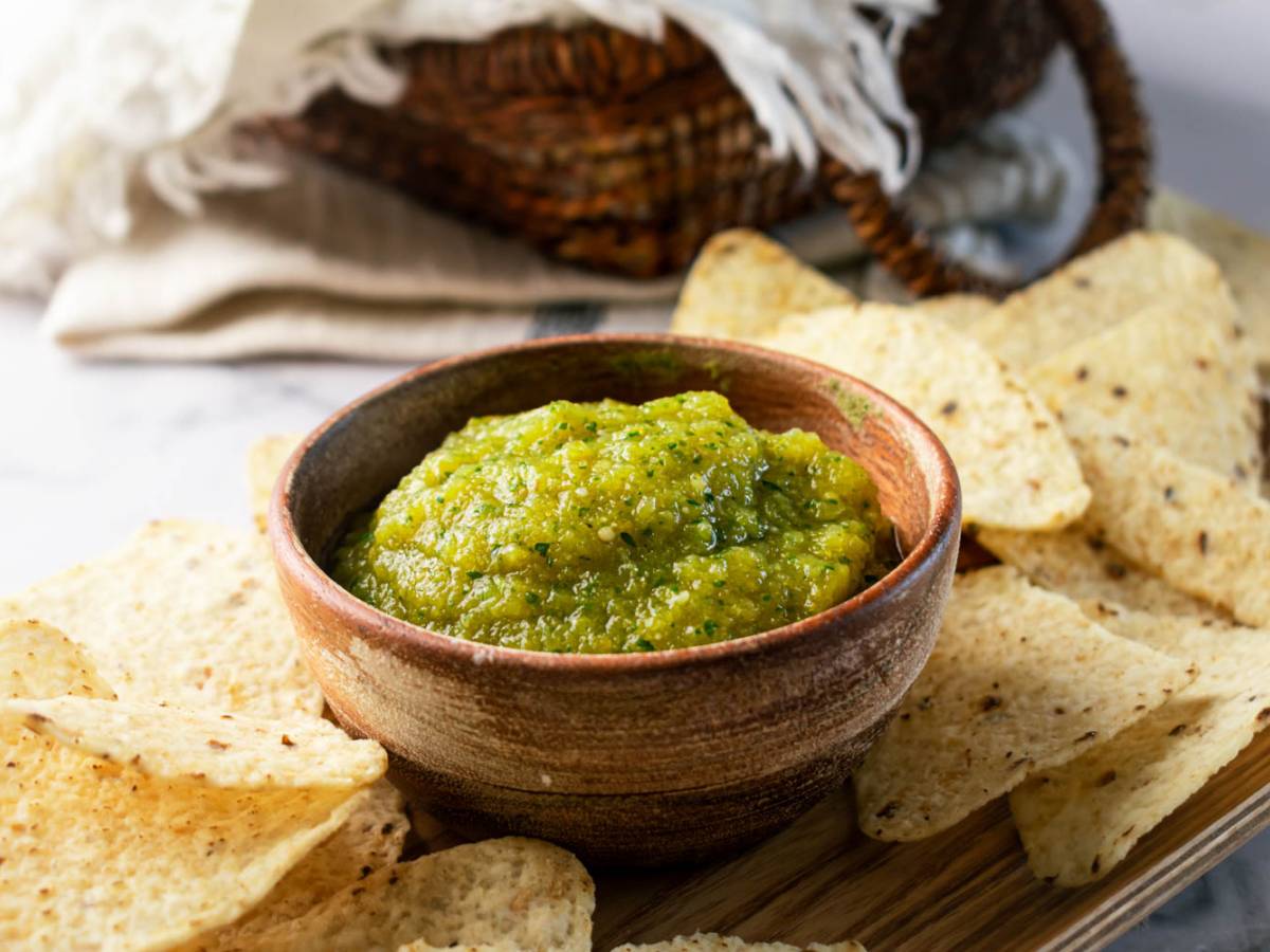Delicious Mexican salsa verde served on a wooden bowl accompanied by crispy tortilla chips.