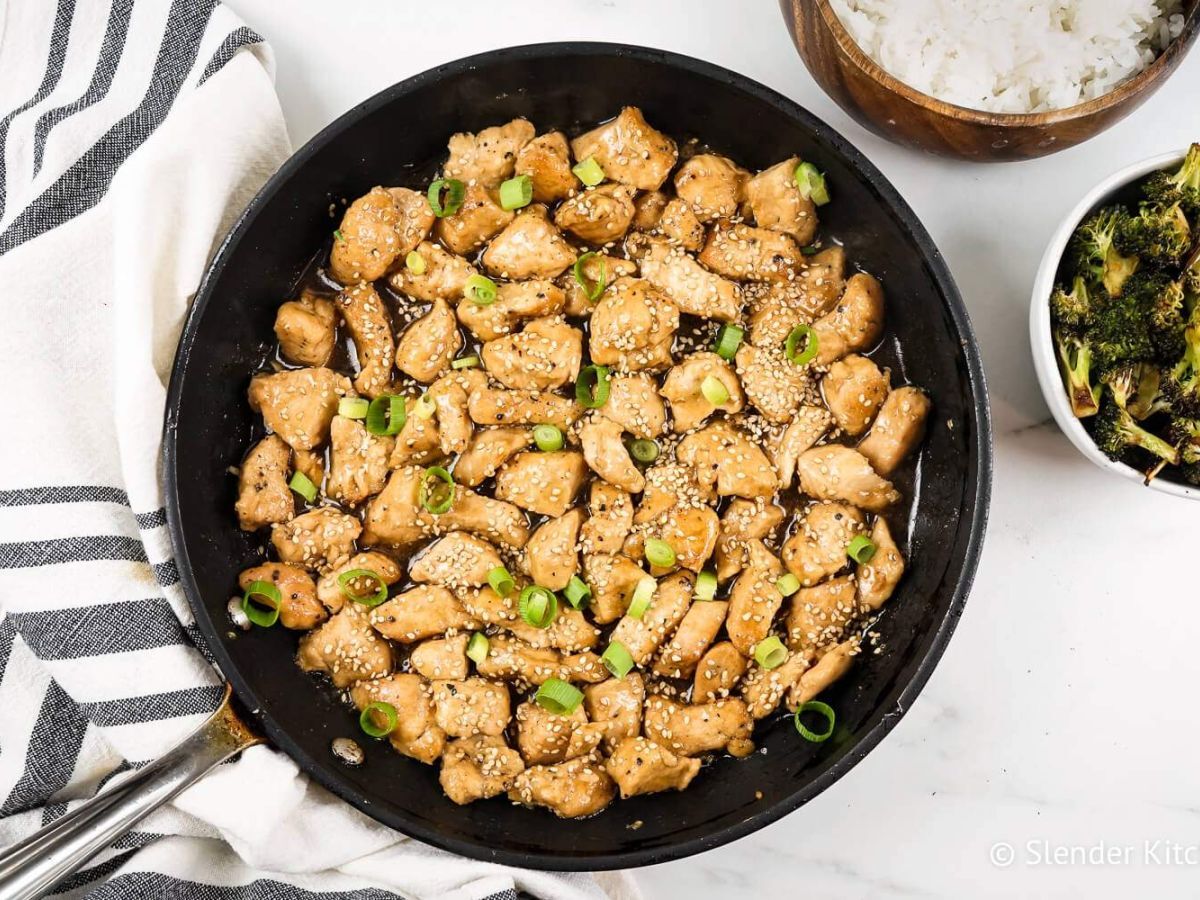 Sesame Chicken in a skillet with green onions with white rice and broccoli on the side.