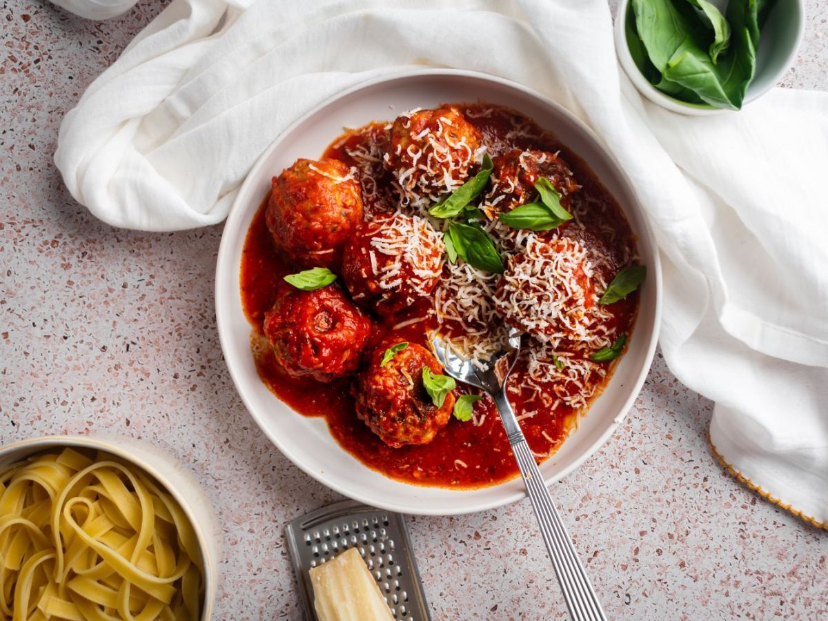 Slow cooker turkey meatballs in a shallow bowl with marinara sauce, fresh basil, and Parmesan cheese. 