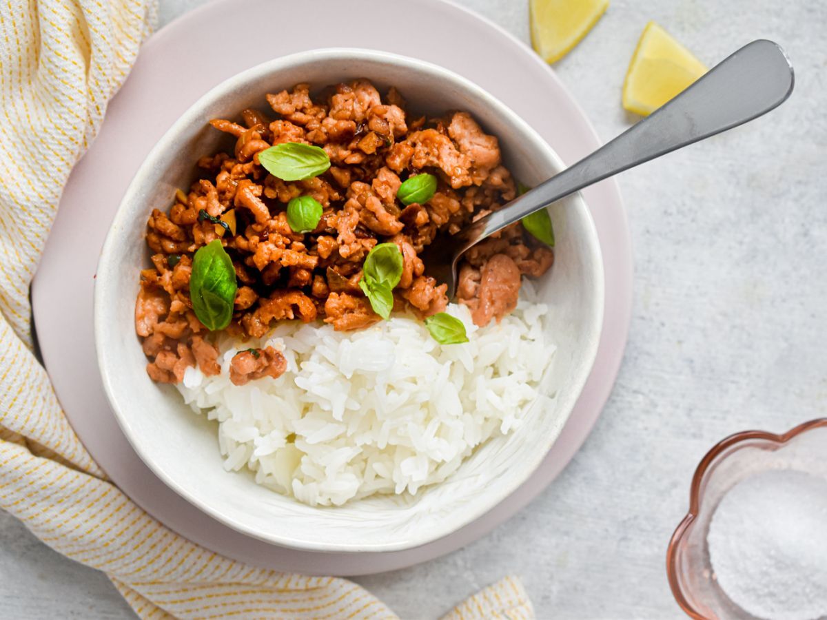 Thai basil ground turkey in a bowl with white rice and Thai basil leaves. 