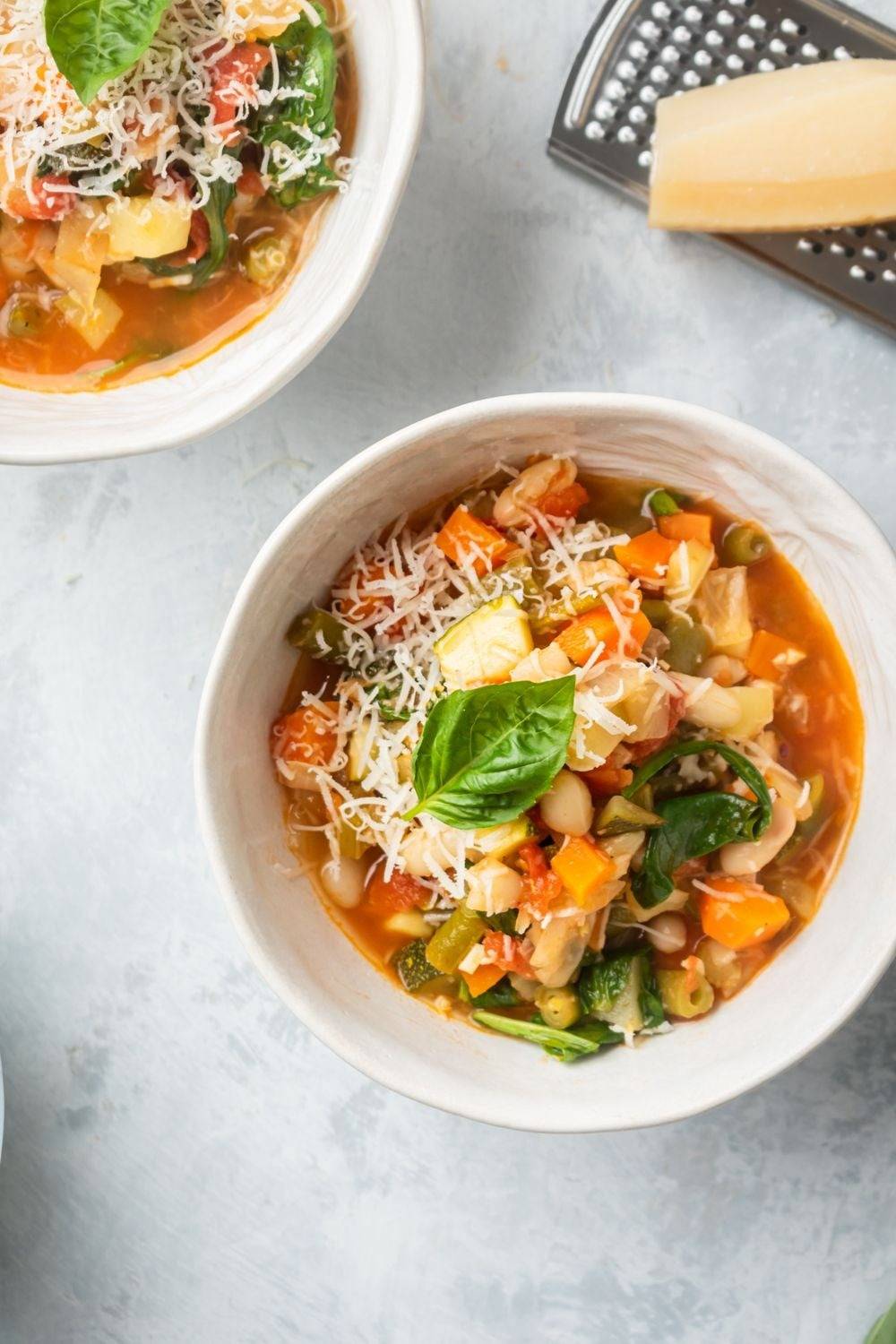 Vegetable and bean soup served in white bowls with basil and parmesan cheese.