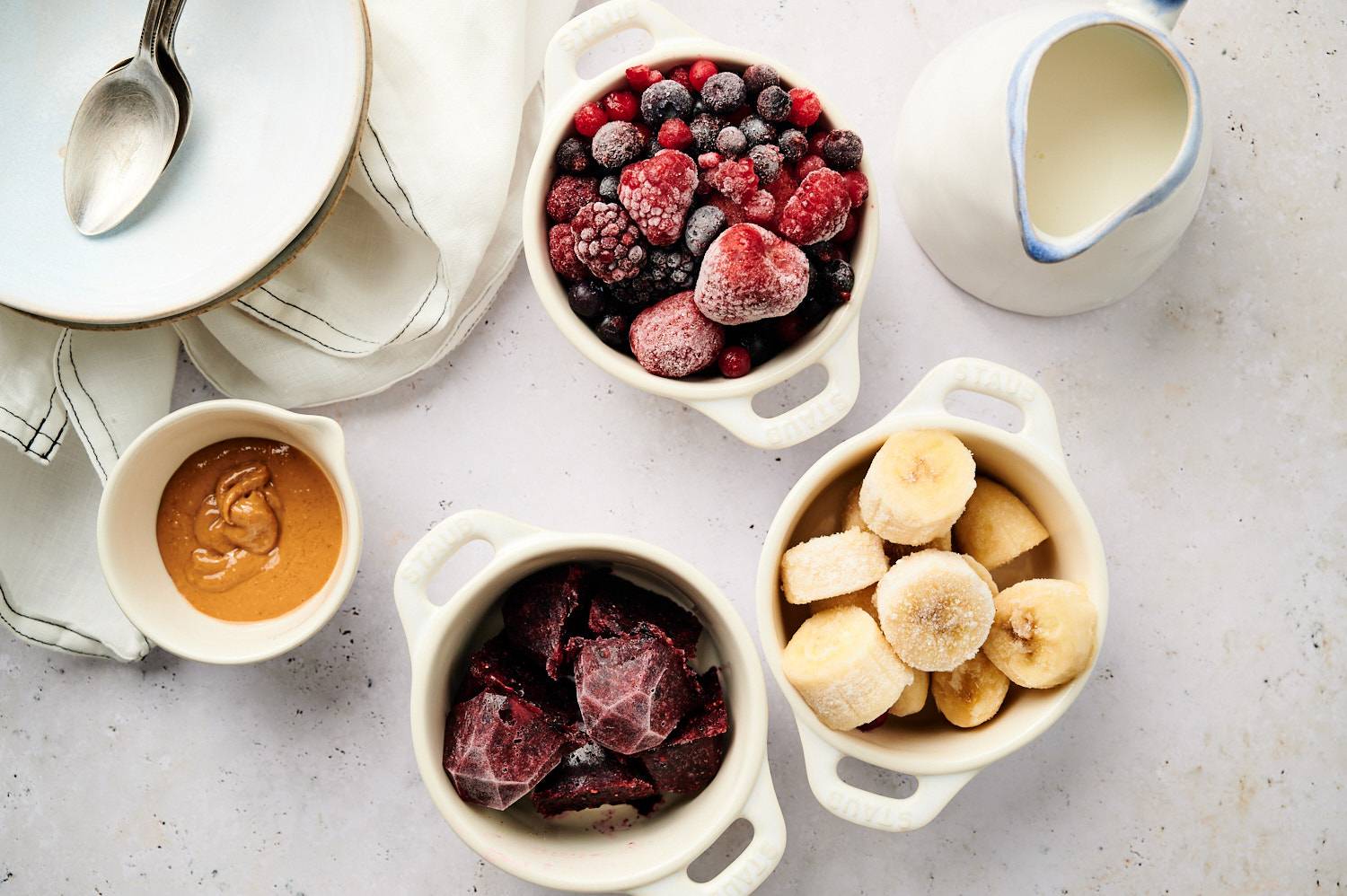 "Acai bowl ingredients in small bowls, including frozen berries, bananas, acai mud, peanut butter and milk.