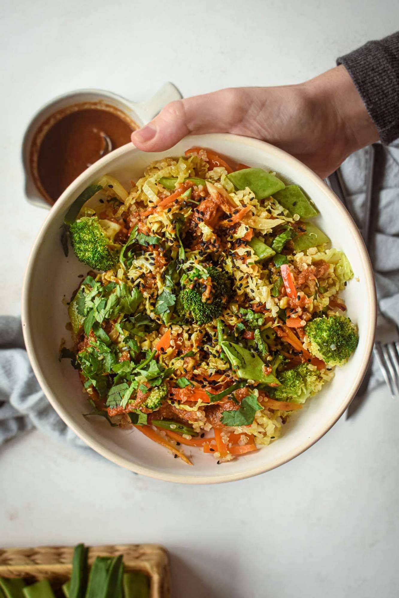 Quinoa in a bowl held in hand with sautéed vegetables in Asian sauce.