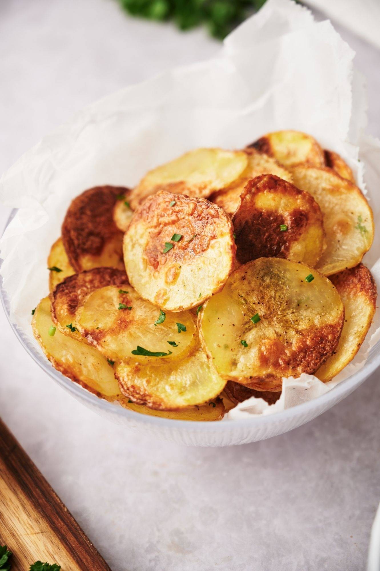 Crispy baked potato chips in a bowl with brown edges and parsley.