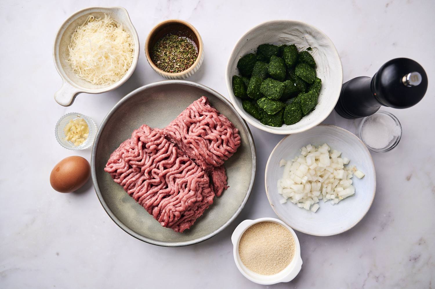 Ingredients for spinach meatballs including ground beef, frozen spinach, onion, garlic, egg, Parmesan cheese, and breadcrumbs.