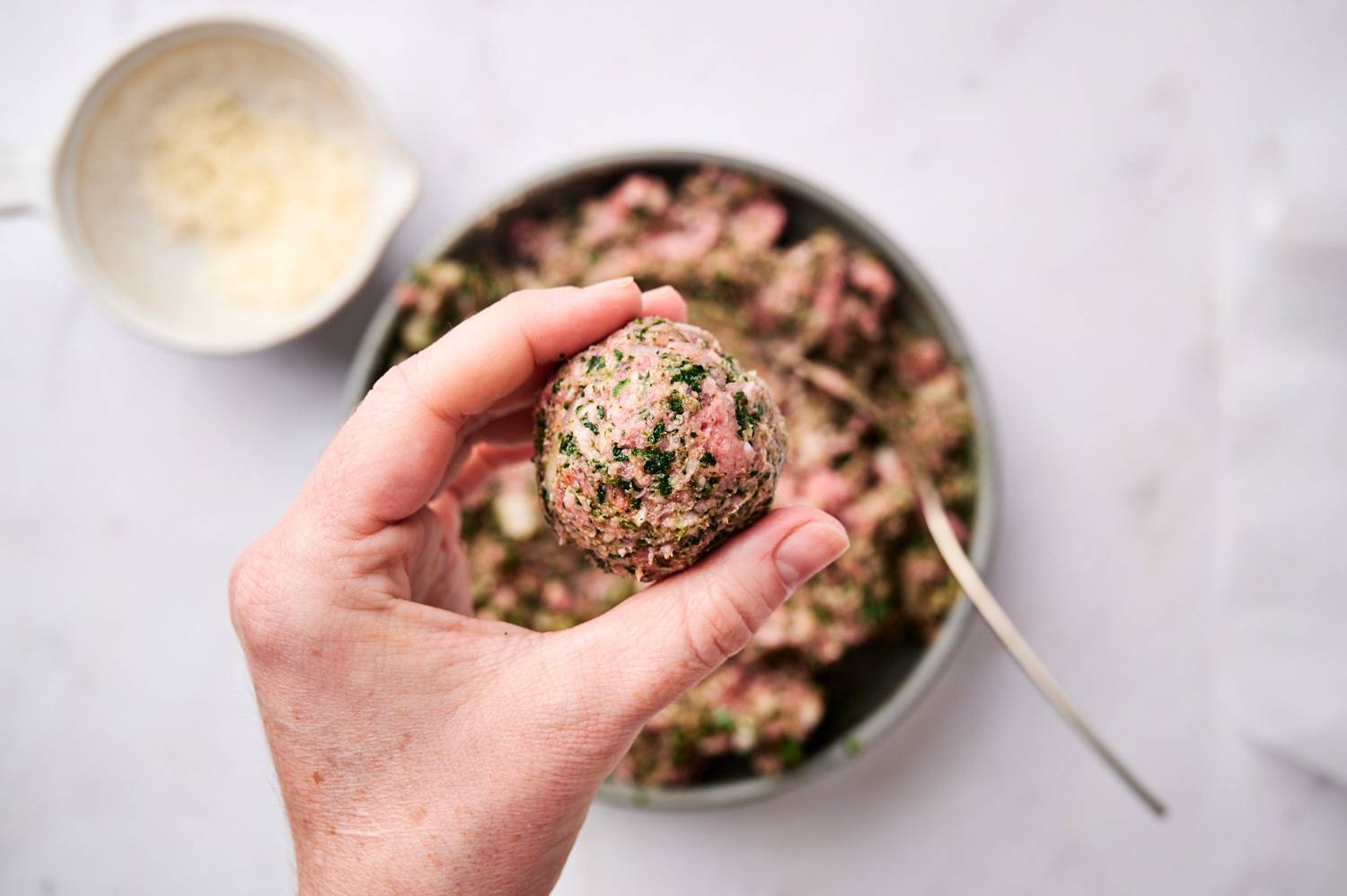 Healthy spinach meatball with ground beef, onion, spinach, and parmesan cheese being held.