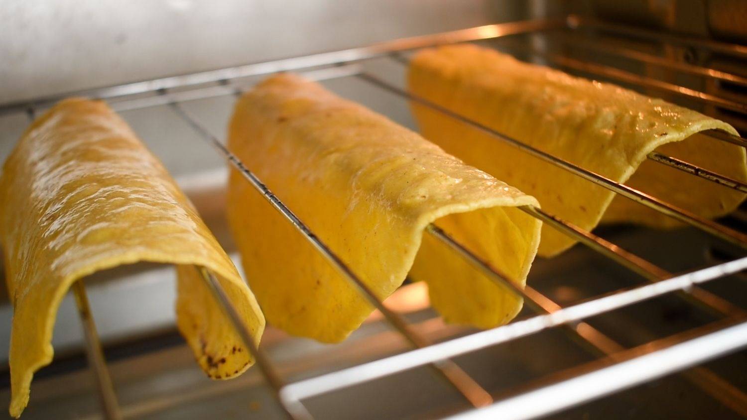 The tortillas are baked in the oven, formed into tortilla shells, and hung on oven racks.