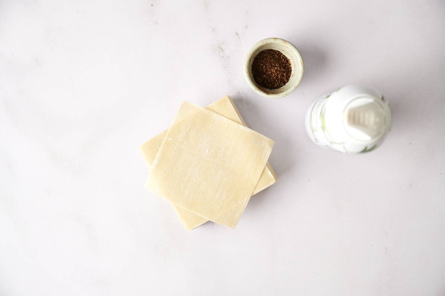 Stack of wonton wrappers on a marble surface with cocoa powder and cooking spray nearby.