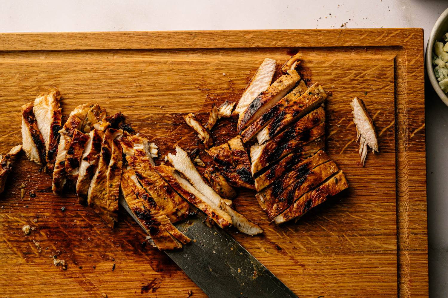 Grilled chicken slices arranged on a wooden cutting board, with a knife placed underneath.