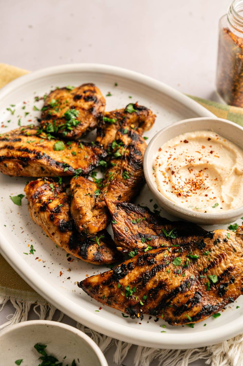 Juicy balsamic grilled chicken with charred grill marks served on a white platter alongside a creamy dipping sauce and fresh parsley garnish.
