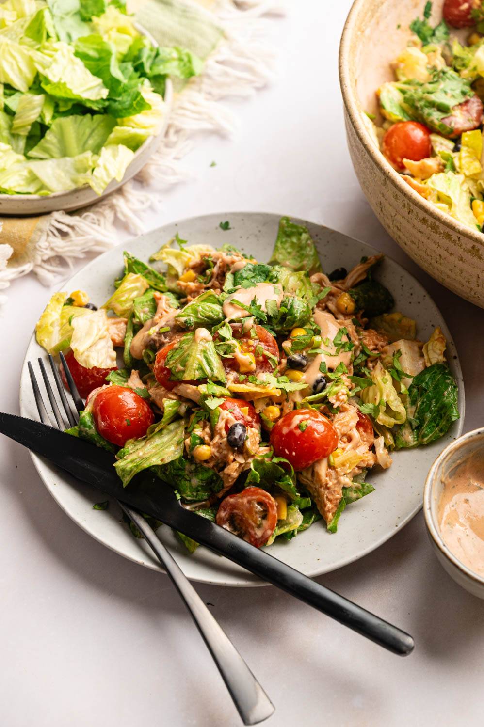 A plate of BBQ chicken chopped salad made with romaine lettuce, barbecue chicken, cherry tomatoes, black beans, corn, and creamy BBQ ranch dressing, served with a fork and knife.
