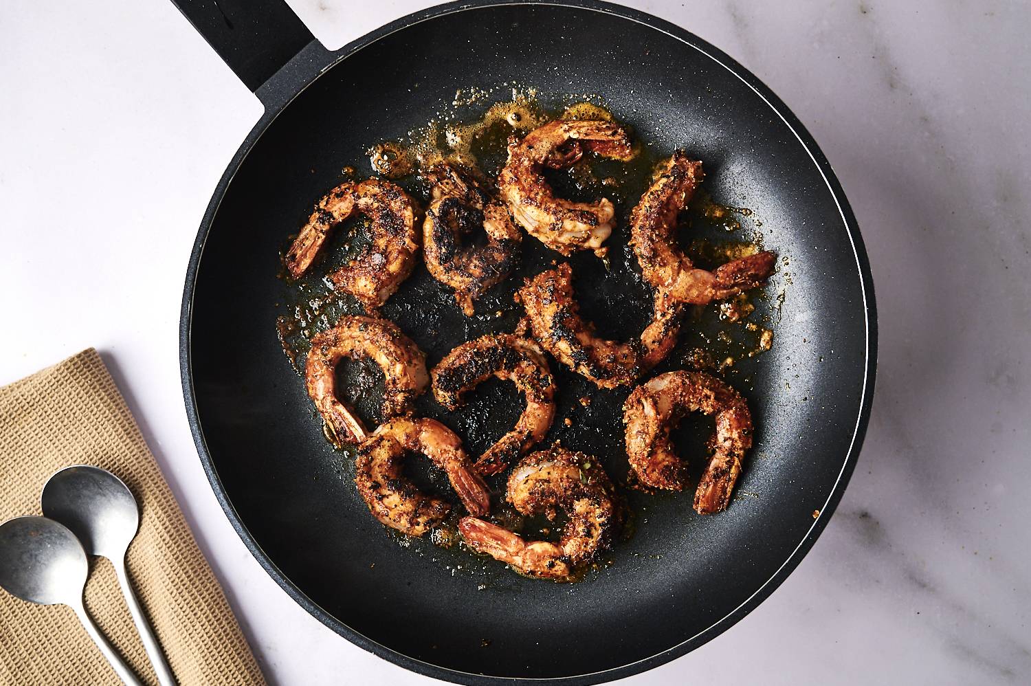 A black skillet filled with perfectly cooked seasoned shrimps, sizzling in golden butter on a marble countertop.