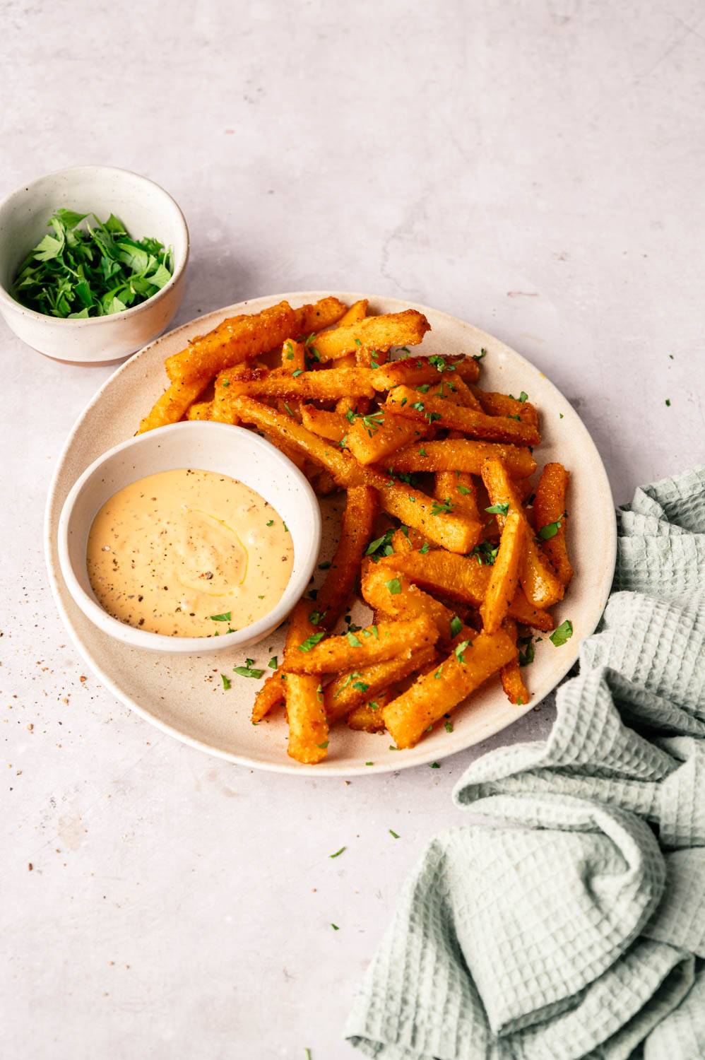 Crispy polenta fries on white plate, garnished with herbs. Serve with creamy dipping sauce and a bowl of fresh parsley. 