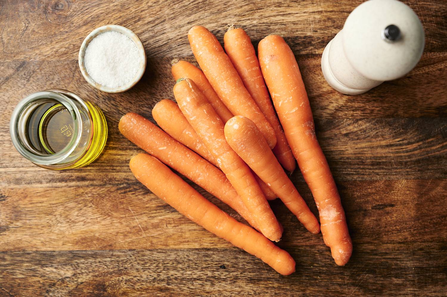 Top-down roasted carrot fries ingredients, including thinly sliced ​​carrots, a bowl of seasoning and a small bowl of olive oil.