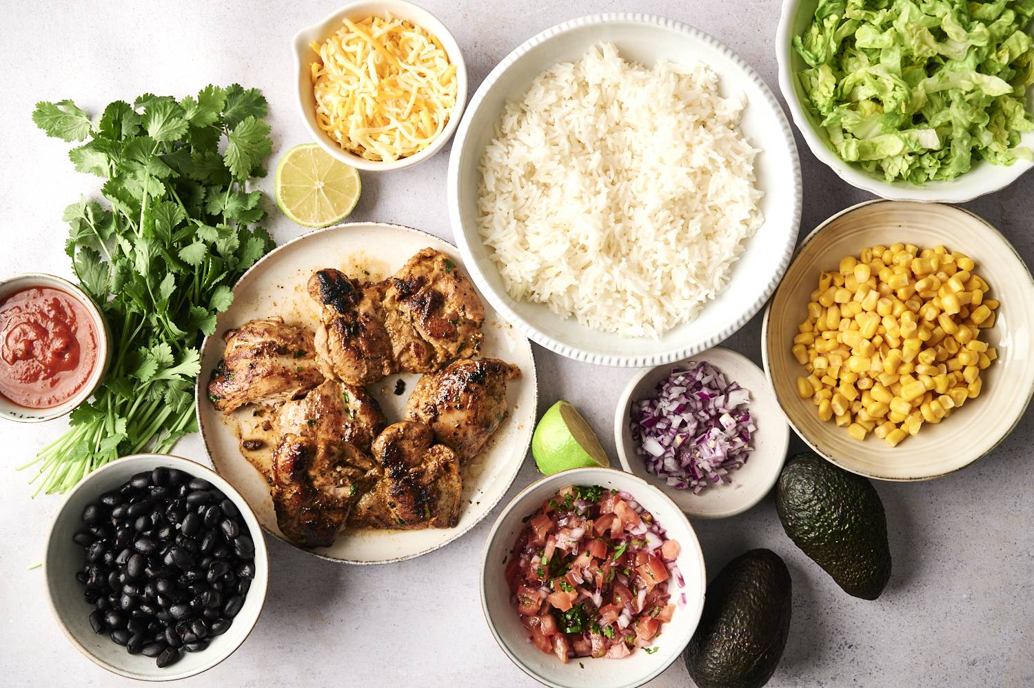 The textured surface is topped with grilled chicken, rice, black beans, corn, lettuce, avocado, salsa, cilantro, cheese and lime.