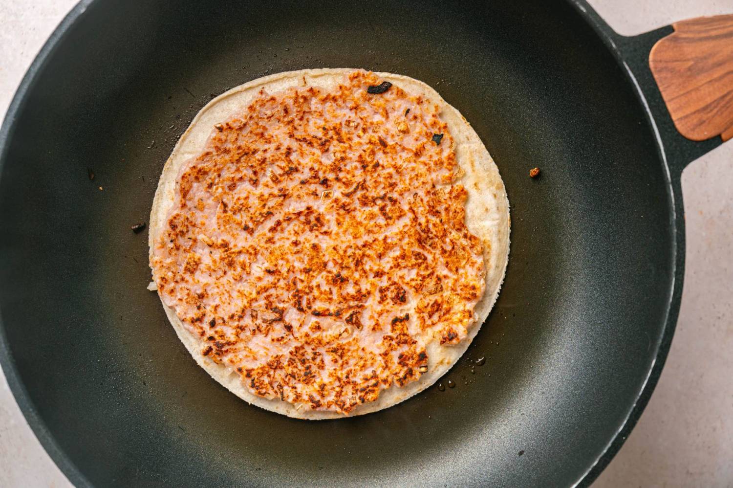 Smashed ground chicken cooked golden brown and crispy on a flour tortilla in a black skillet.