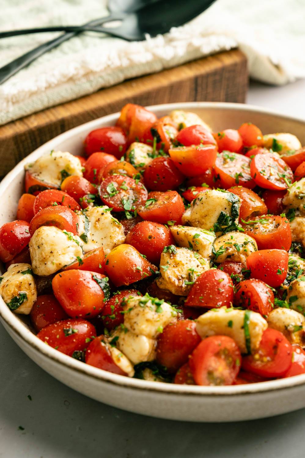 Close-up of chopped Caprese salad with fresh mozzarella, cherry tomatoes, basil, olive oil, and balsamic glaze in a serving bowl.