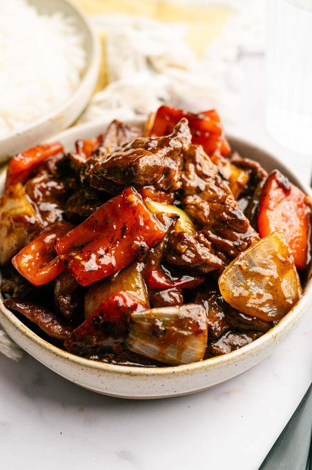 A bowl of sizzling beef stir-fry with vibrant red peppers and onions, glazed in rich sauce.