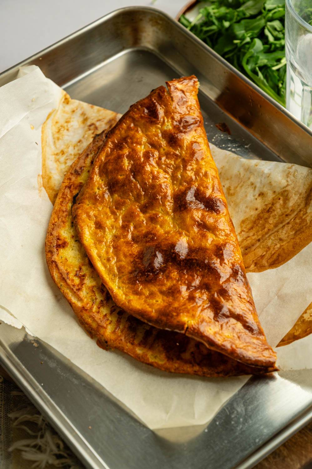 Golden brown cottage cheese flatbread folded in half and resting on parchment paper in a baking pan.