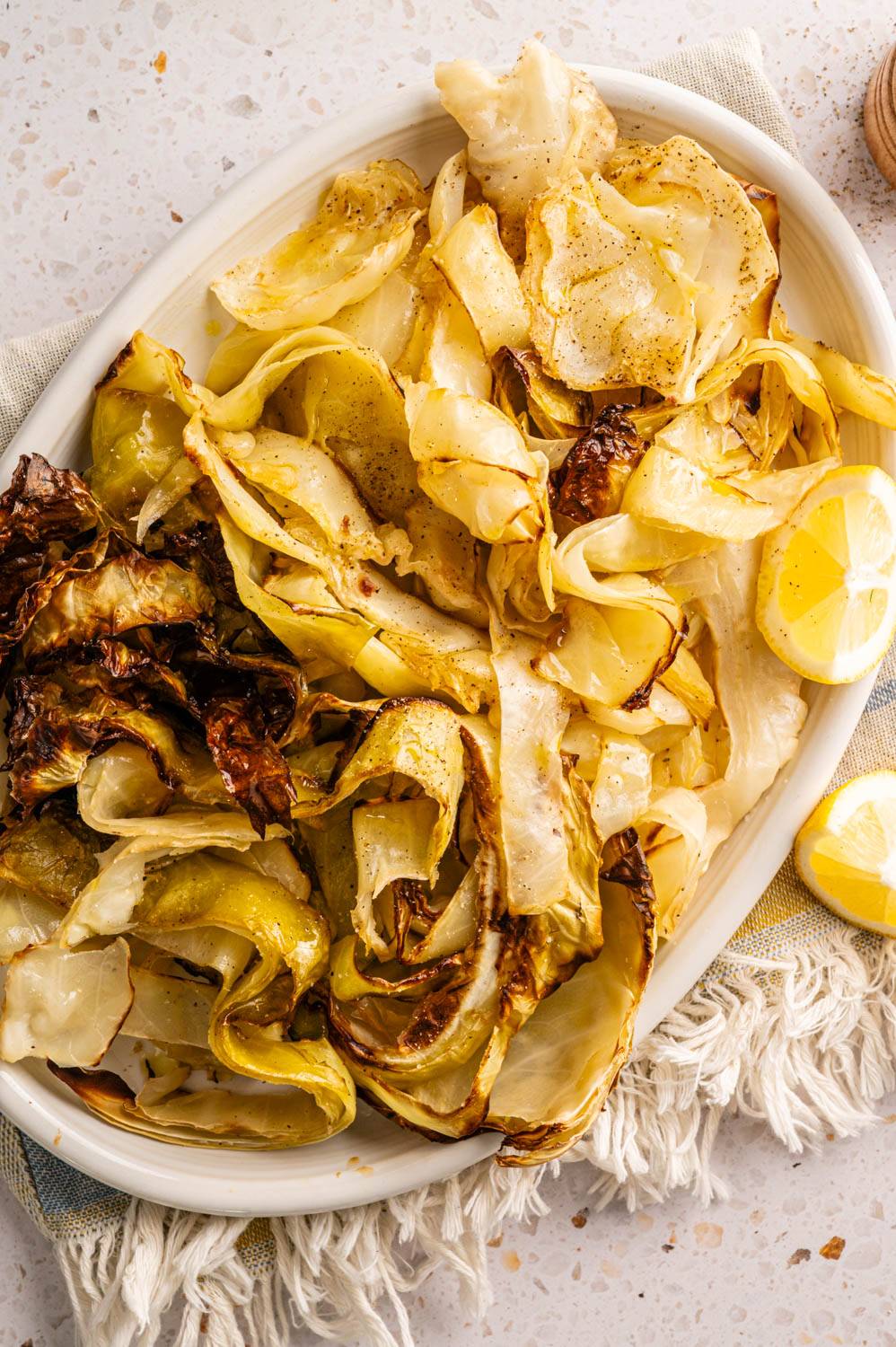 Roasted cabbage slices on a white oval platter, seasoned with pepper and garnished with lemon wedges.