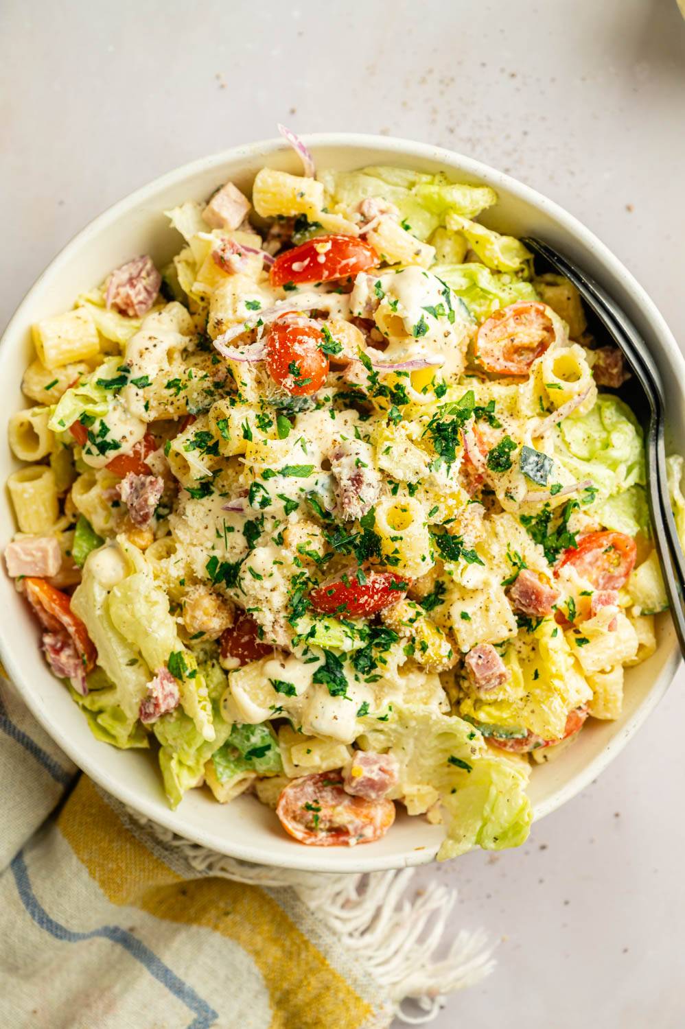 Creamy Italian pasta salad served on a plate with ditalini pasta, lettuce, tomatoes, chickpeas, deli meats, and Parmesan, garnished with fresh herbs.