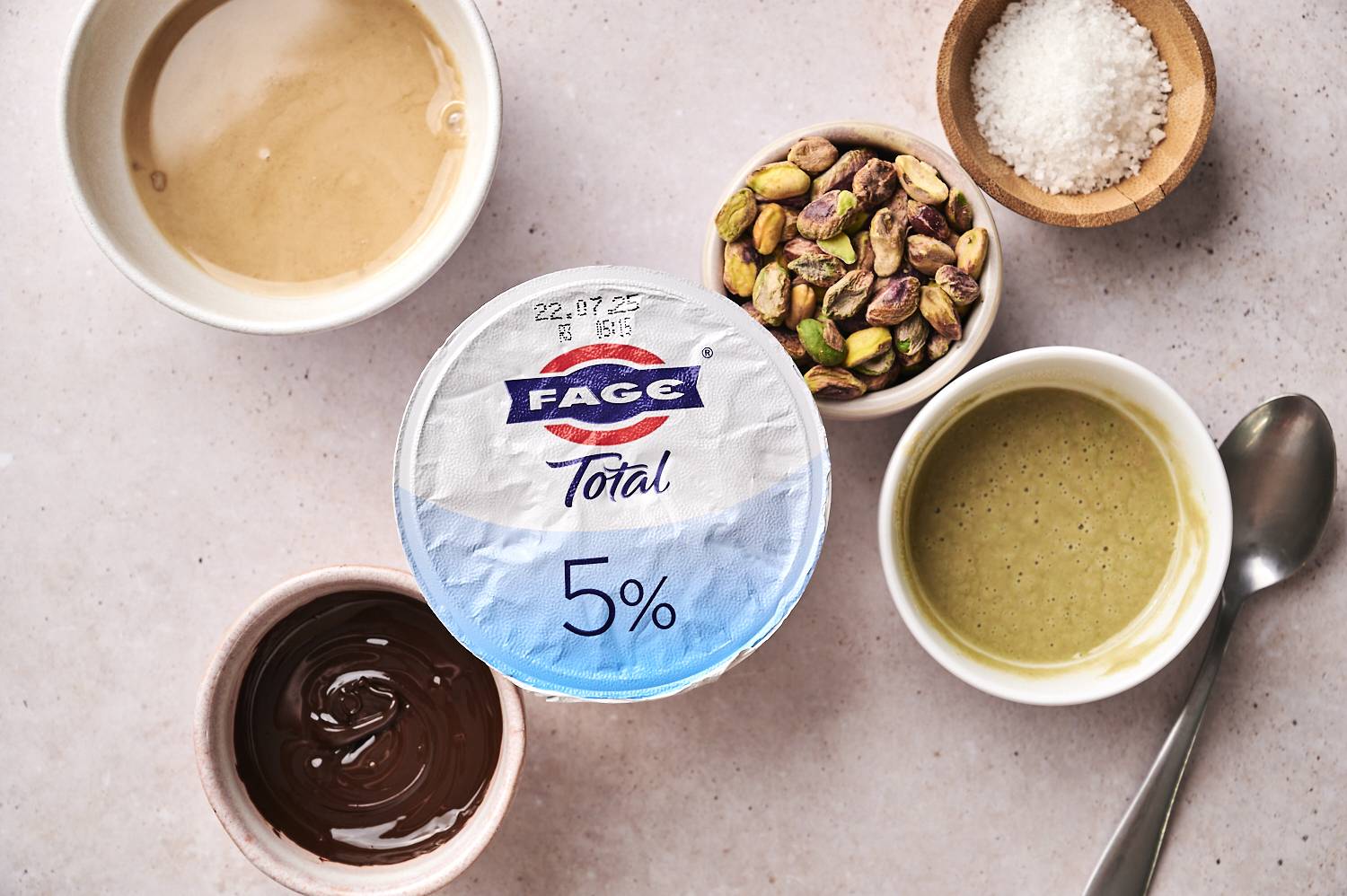 Top-down Dubai chocolate yogurt cup ingredients, including a bowl of dates and various nuts.