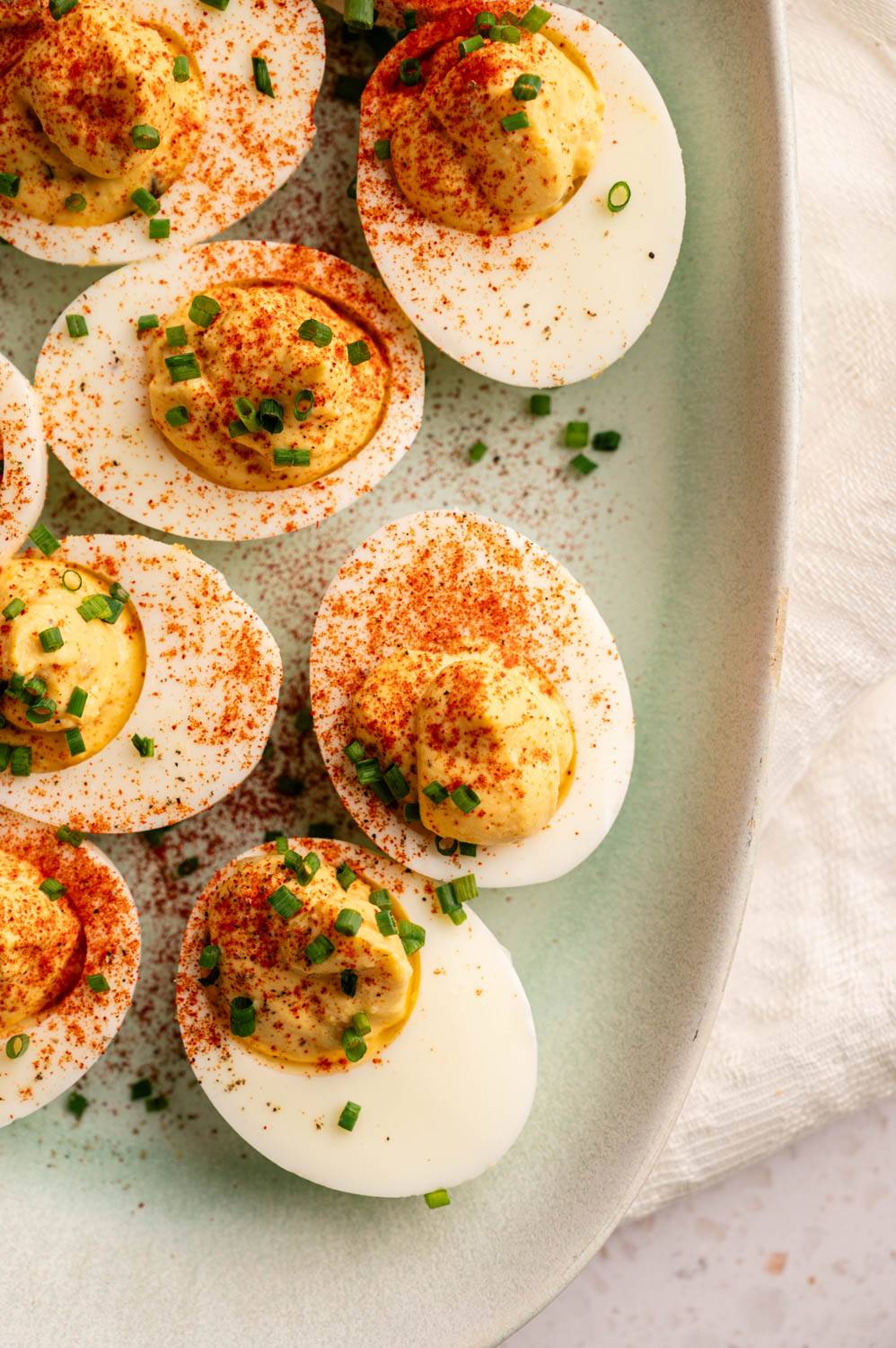 Close-up of deviled eggs on light green plate, garnished with paprika and chopped chives. The eggs have a creamy yellow filling.