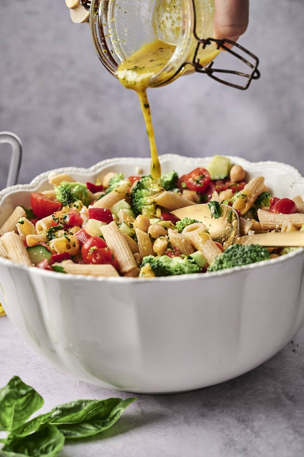 Pour vibrant yellow seasonings in one hand in a colorful pasta, cherry tomatoes, broccoli and chickpeas, in a large white bowl.
