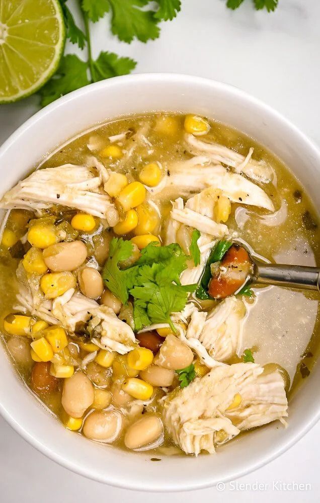 Healthy Chicken Chili with chicken breast, beans, cilantro and lime in a white bowl.
