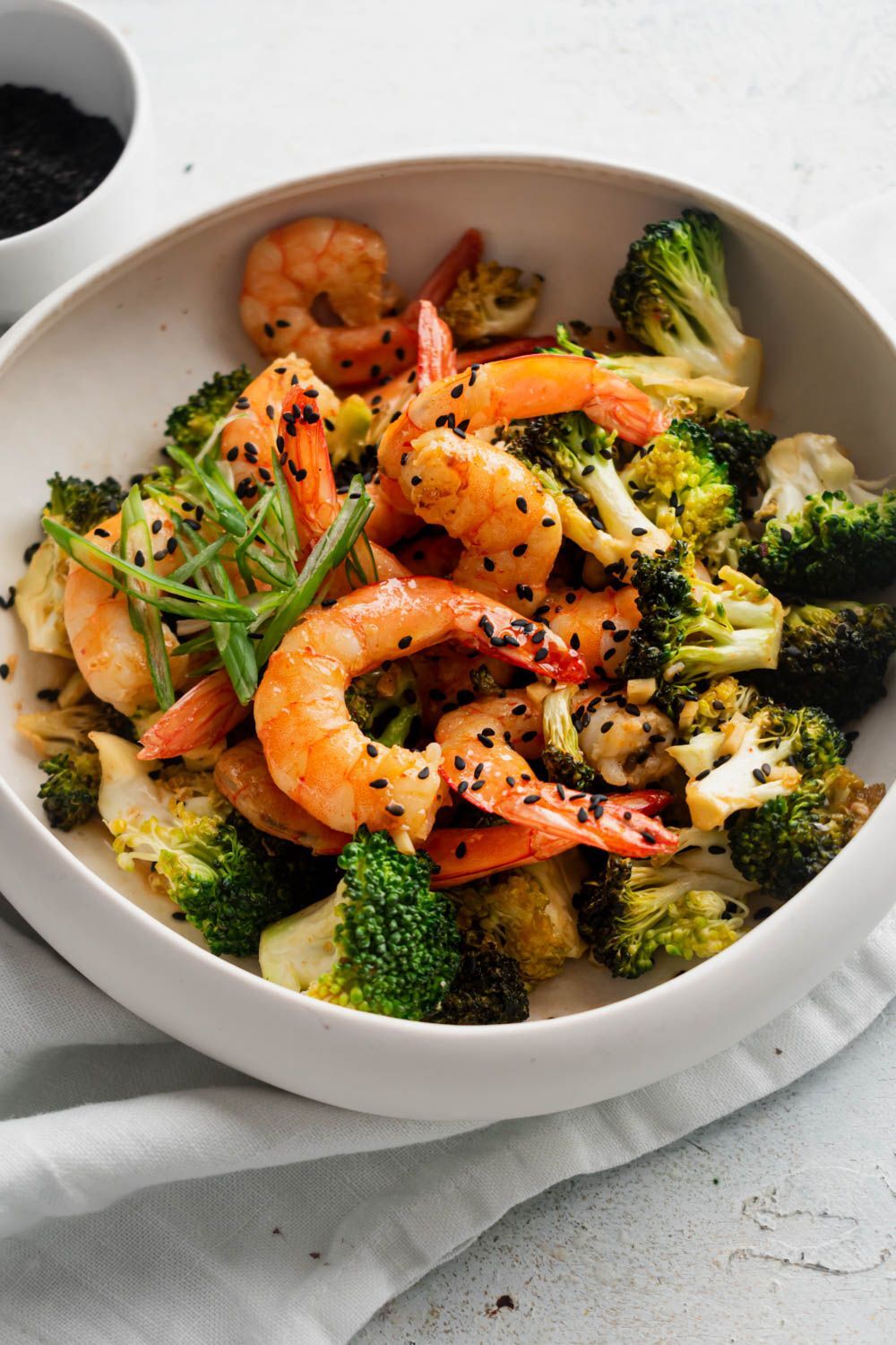 Serve broccoli, green onion and firecracker shrimp in black sesame seeds in a white bowl in a slightly spicy sauce.