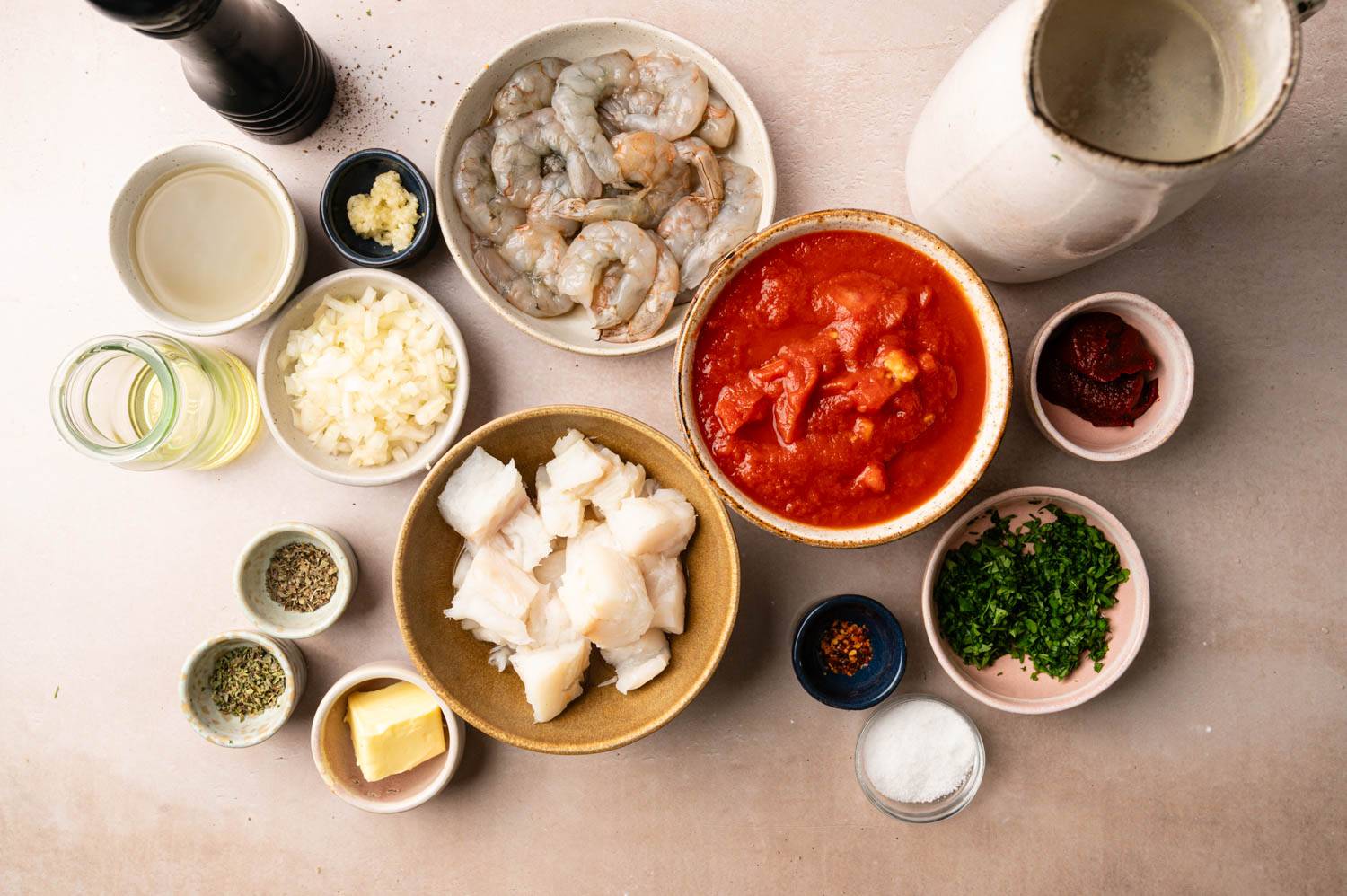 Ingredients for a seafood dish on the table: raw shrimps, fish pieces, tomato sauce, chopped herbs, onions, garlic, spices, butter and broth. Cooking preparation.
