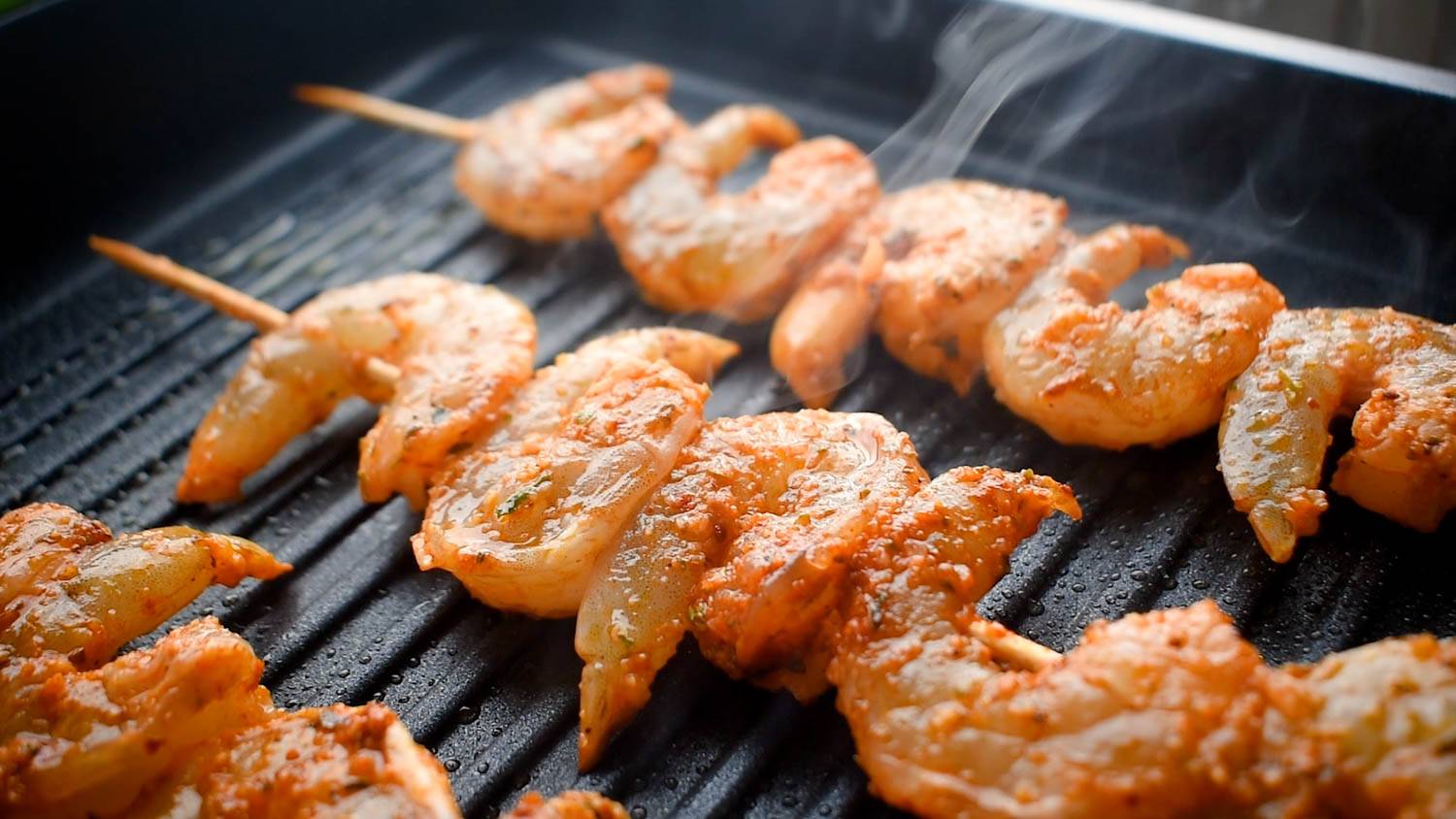 Grilled shrimp skewers sizzle on the hot grill, coated with spices, steam rising in the background.