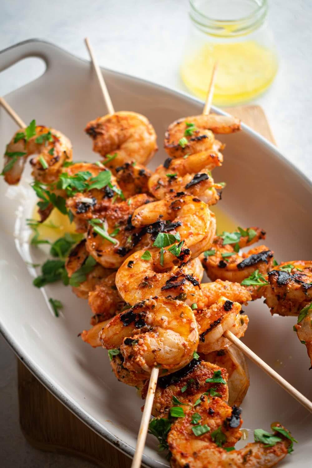 Grilled shrimp skewers on a white plate with fresh parsley on the background accompanied by a can of yellow sauce.