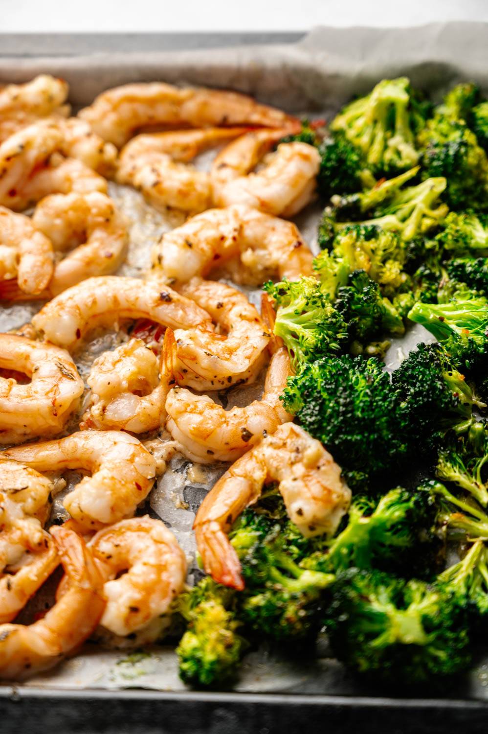 Grilled shrimp seasoned with spices served alongside roasted broccoli on a parchment-lined baking sheet conveys a fresh and appetizing meal.