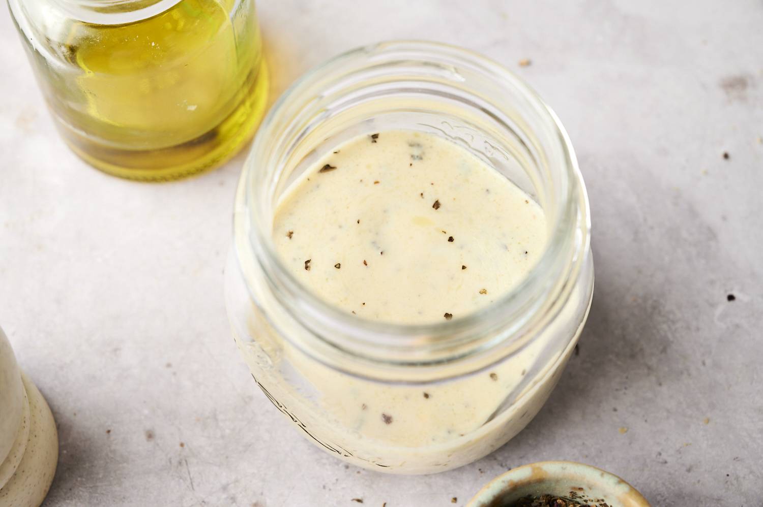 Close-up of creamy Greek salad dressing in glass jar, sprinkled with black pepper.