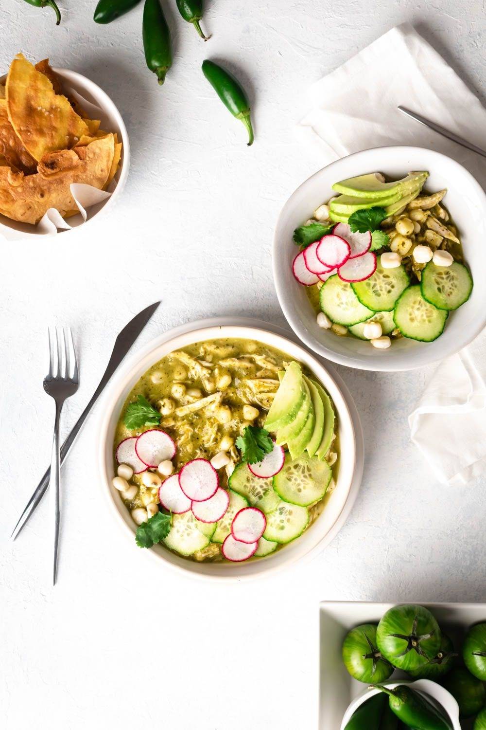 Green chicken side dish is served in two bowls with chopped chicken, hominy, green soup, abaccardo and carrots sliced.
