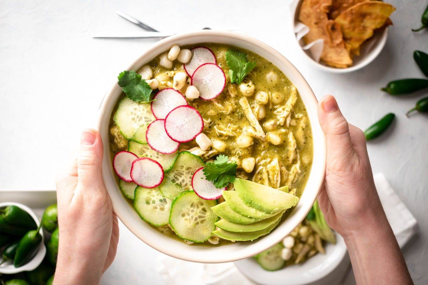 Pozole verde is placed in a bowl with chicken with radish, coriander, avocado, Hominy and Cucumbers.