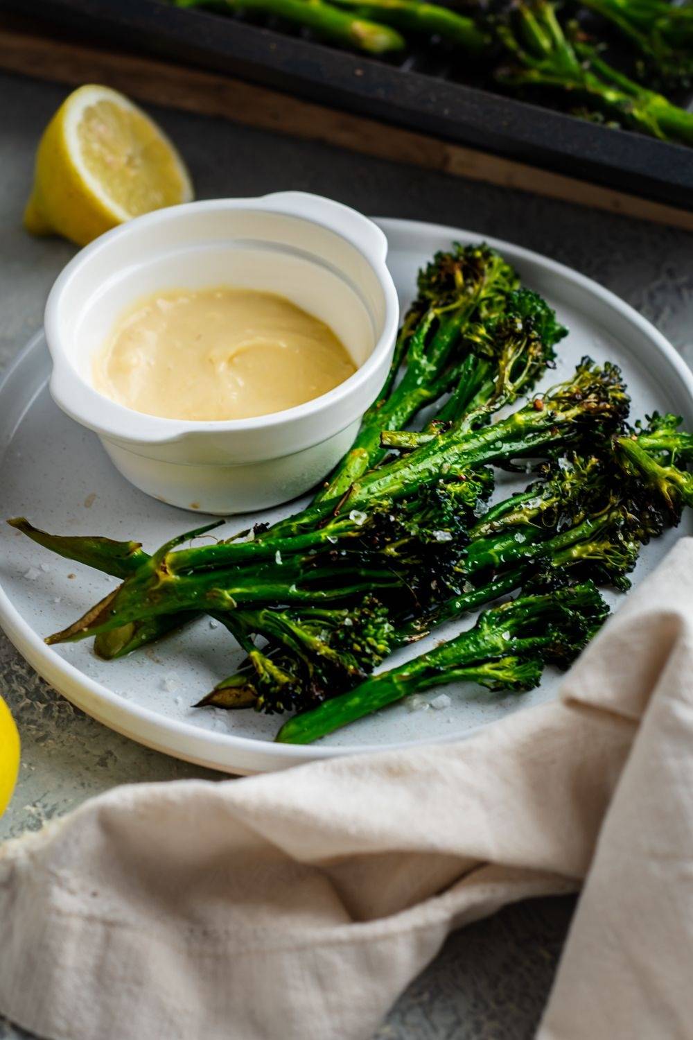 Roasted broccoli and burnt edges on a plate with lemon and garlic dipping sauce.