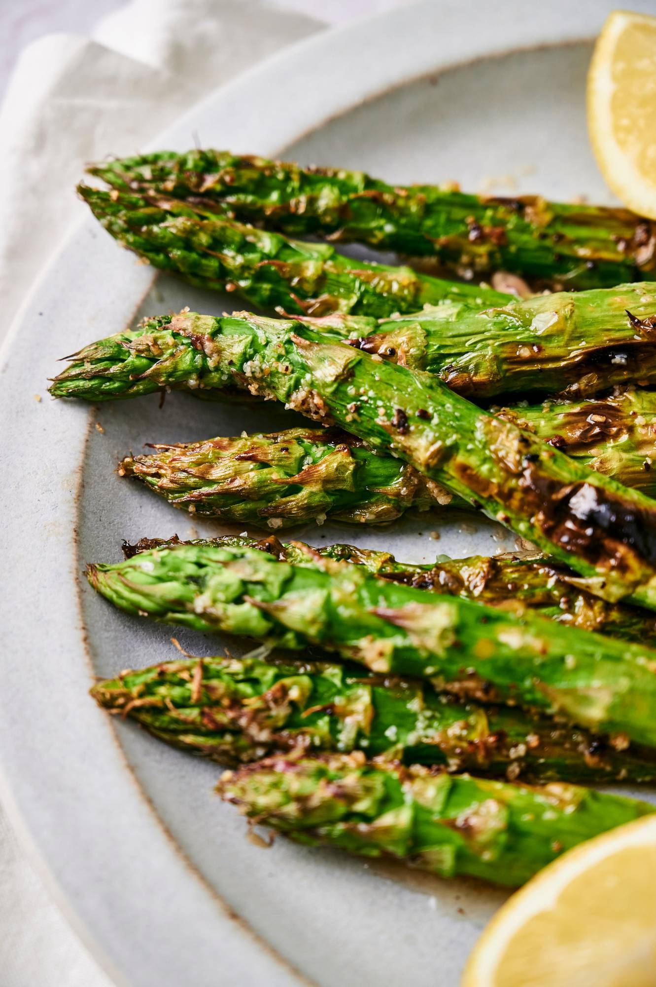 Plate of grilled asparagus with lemons, salt, and pepper.