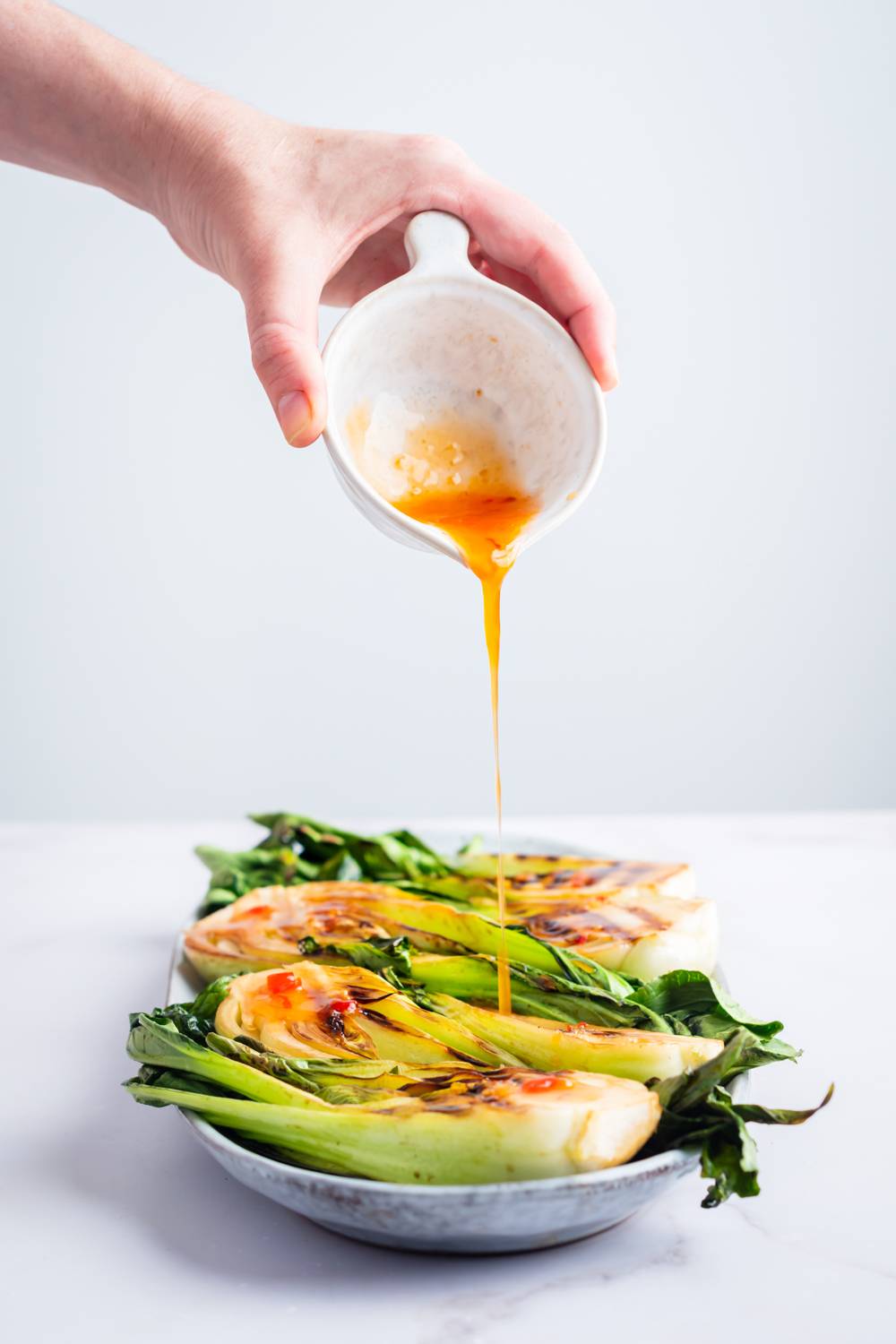 Pour a savory sauce of grilled jam on a white marble surface with vibrant vegetables on top.