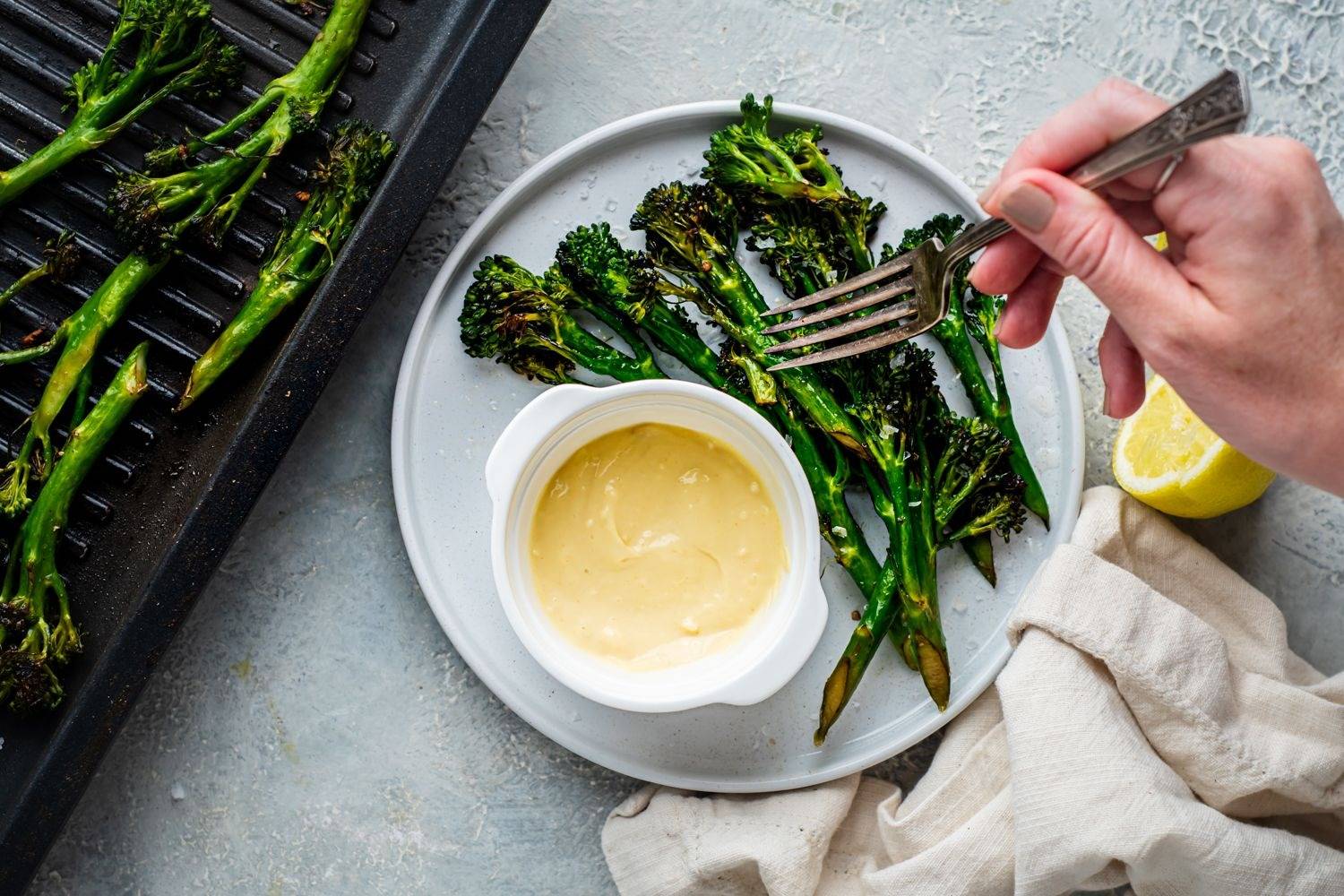 Crispy roasted broccoli on a plate and on a roasting pan with lemon, garlic aioli and black pepper.