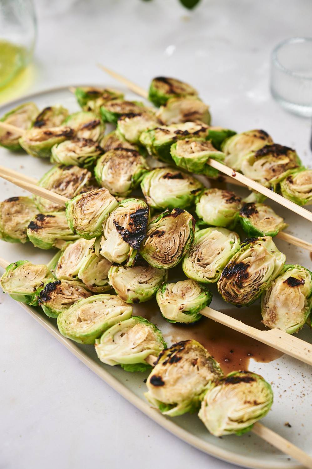 Burnt Brussels sprouts put on the skewers and paired on a neutral plate with sparkling edges and sauce splashed below.