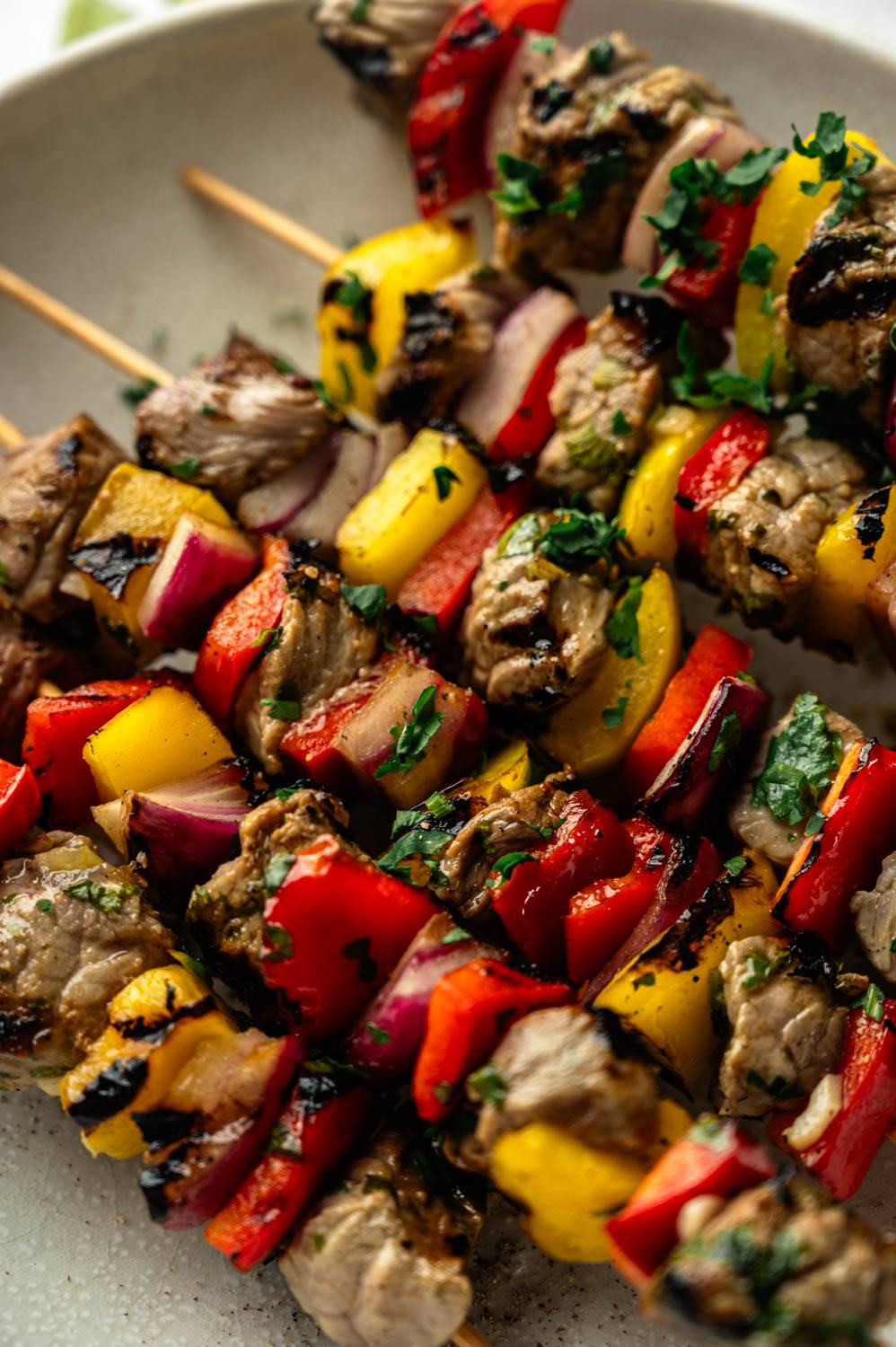 Close-up of grilled steak and vegetable skewers on a plate, showing charred steak cubes alternating with red and yellow bell pepper and red onion pieces, flecked with chopped cilantro.
