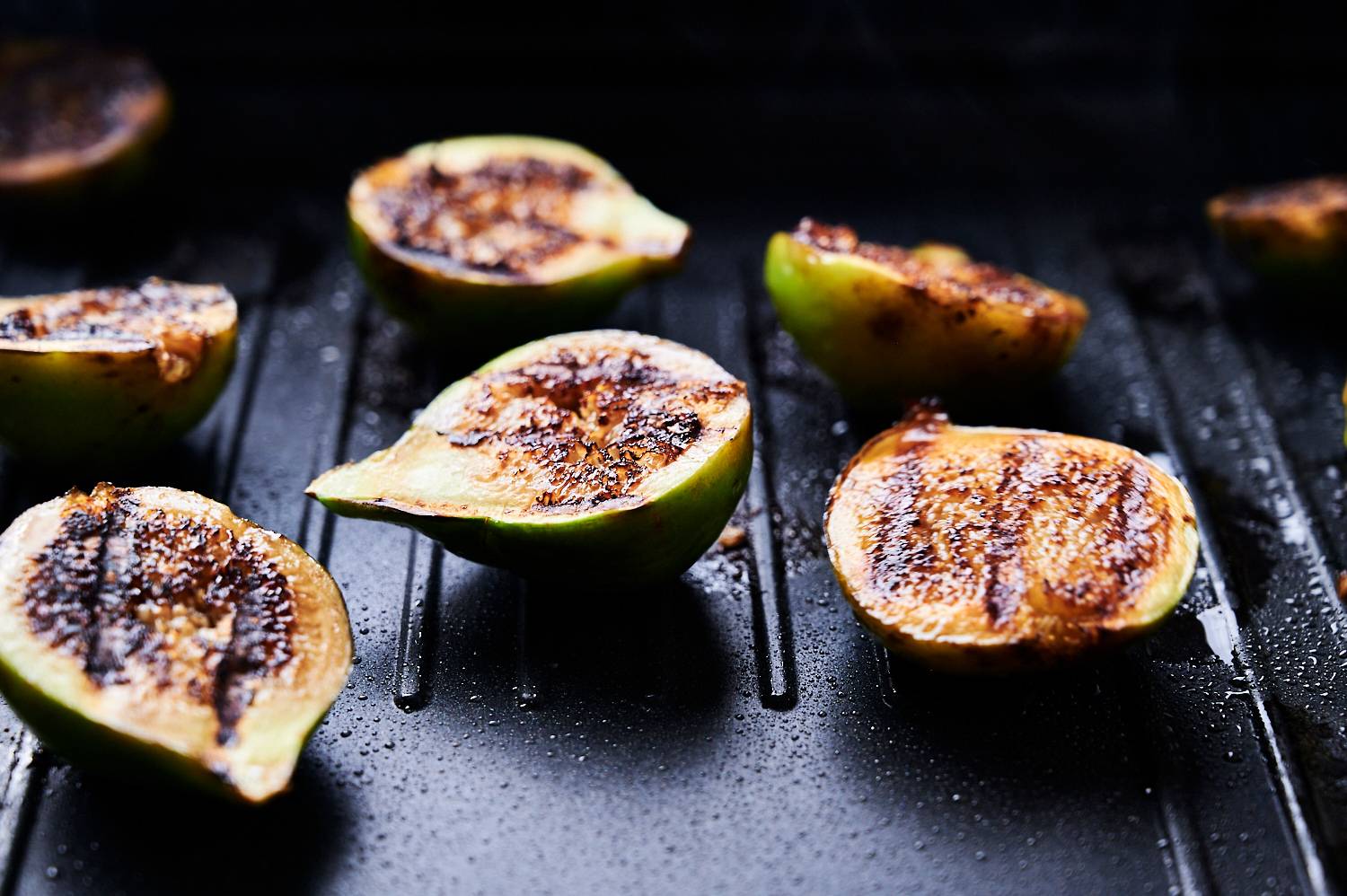 Charred grilled figs on a grill with caramelized edges.